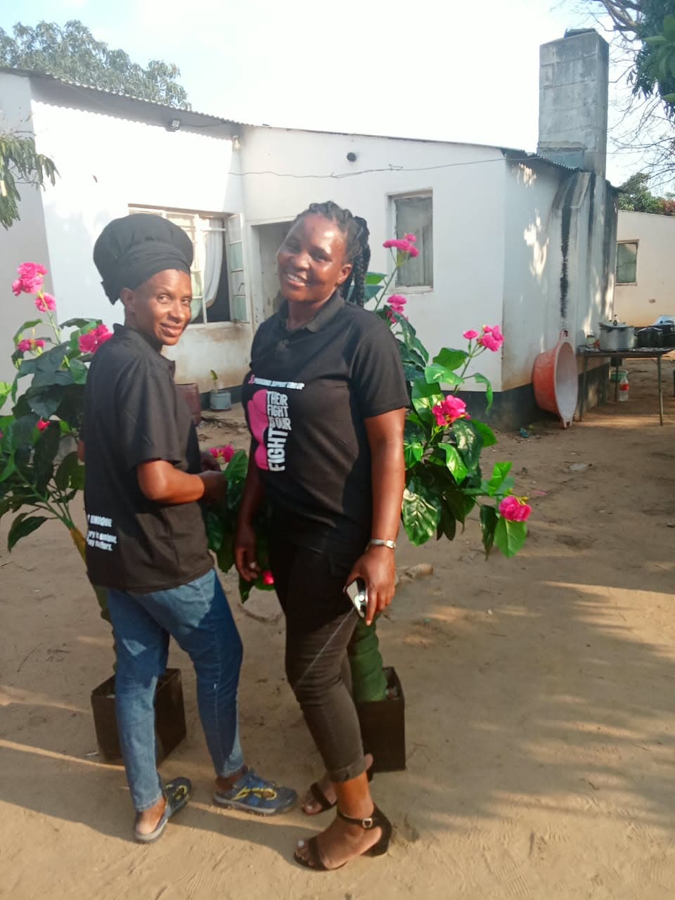 Two women wearing awareness shirts beside flowering plants