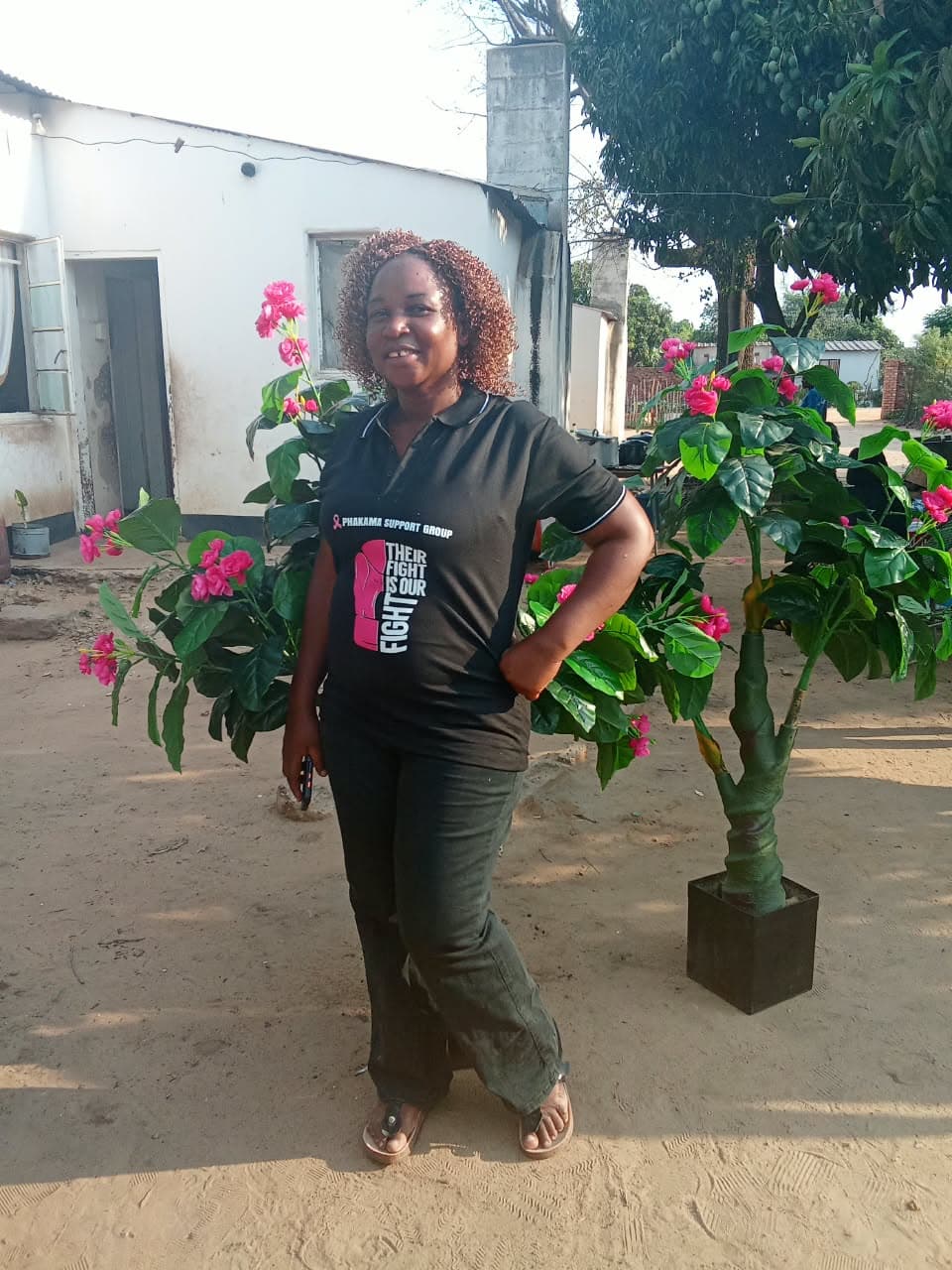 A woman in a breast cancer awareness shirt beside pink flowers
