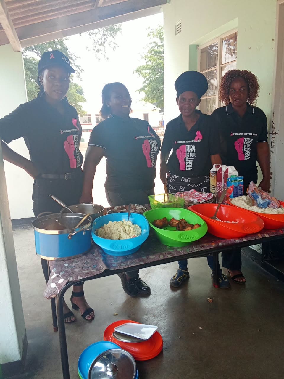 Women in awareness shirts standing beside a table of shared food